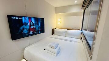 Una habitación de hotel con una cama, un televisor montado en la pared y una mesita de noche.