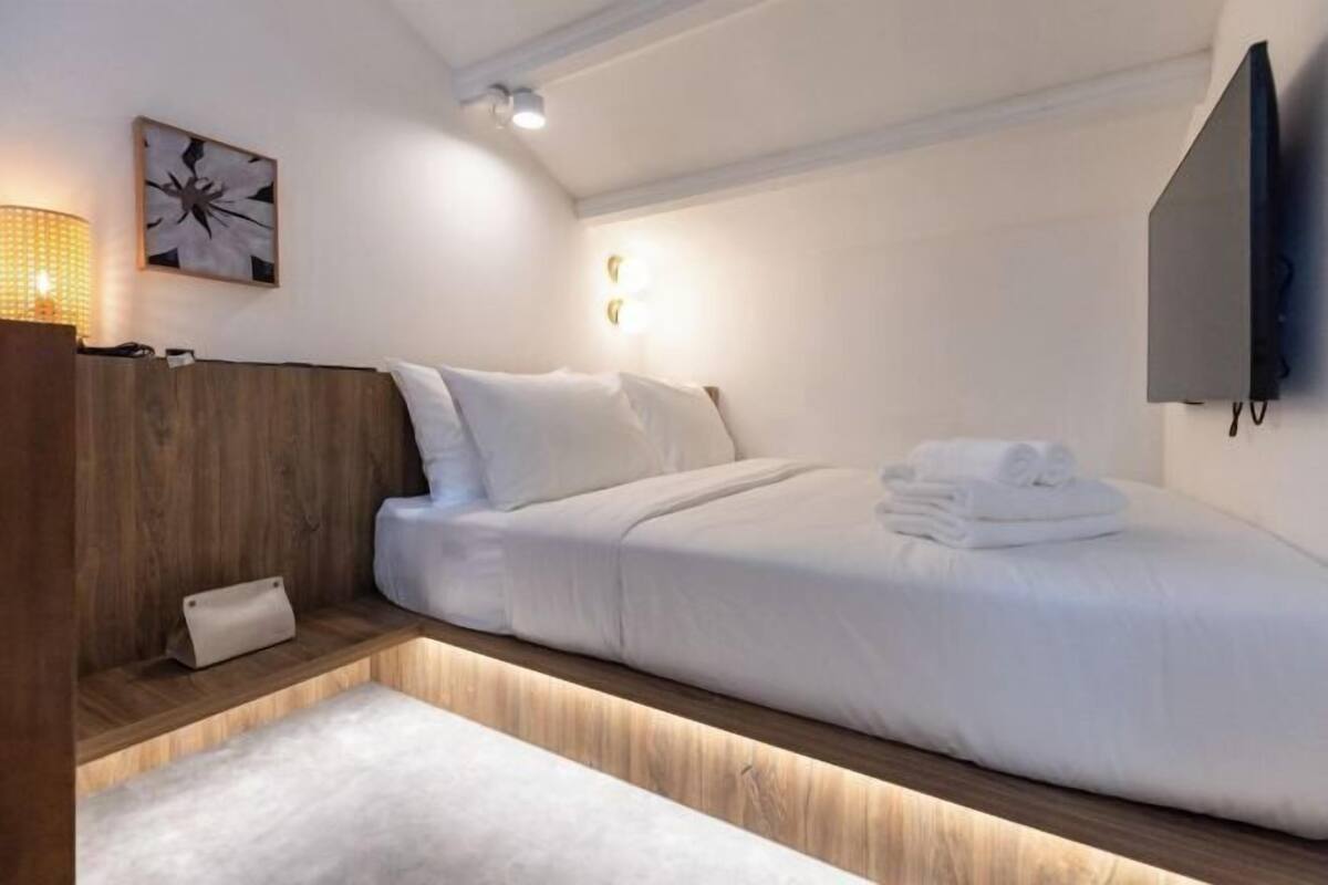 A modern hotel room with a bed, bedside table, lamp, artwork, and a flat-screen TV.
