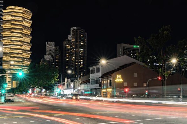A nighttime cityscape with illuminated buildings, a street with light trails from vehicles, and a prominent hotel with a sign. - Heritage Collection on Victoria - Mobile App Check-In (Singapore)