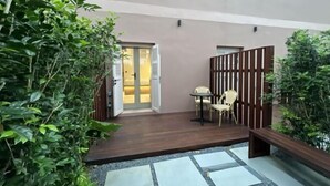 Une cour avec une terrasse en bois, une petite table entourée de chaises et une porte donnant sur une pièce.