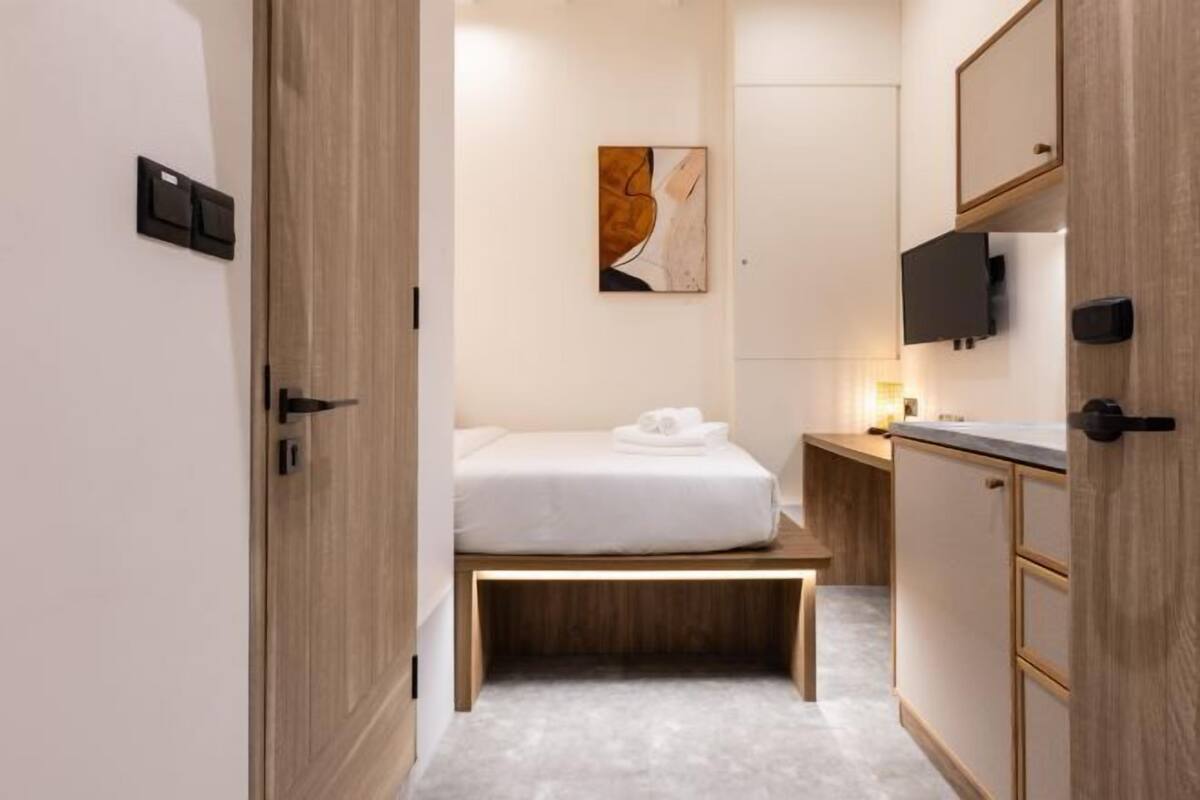 A modern hotel room with a bed, a wooden bench, a TV, and a painting on the wall.