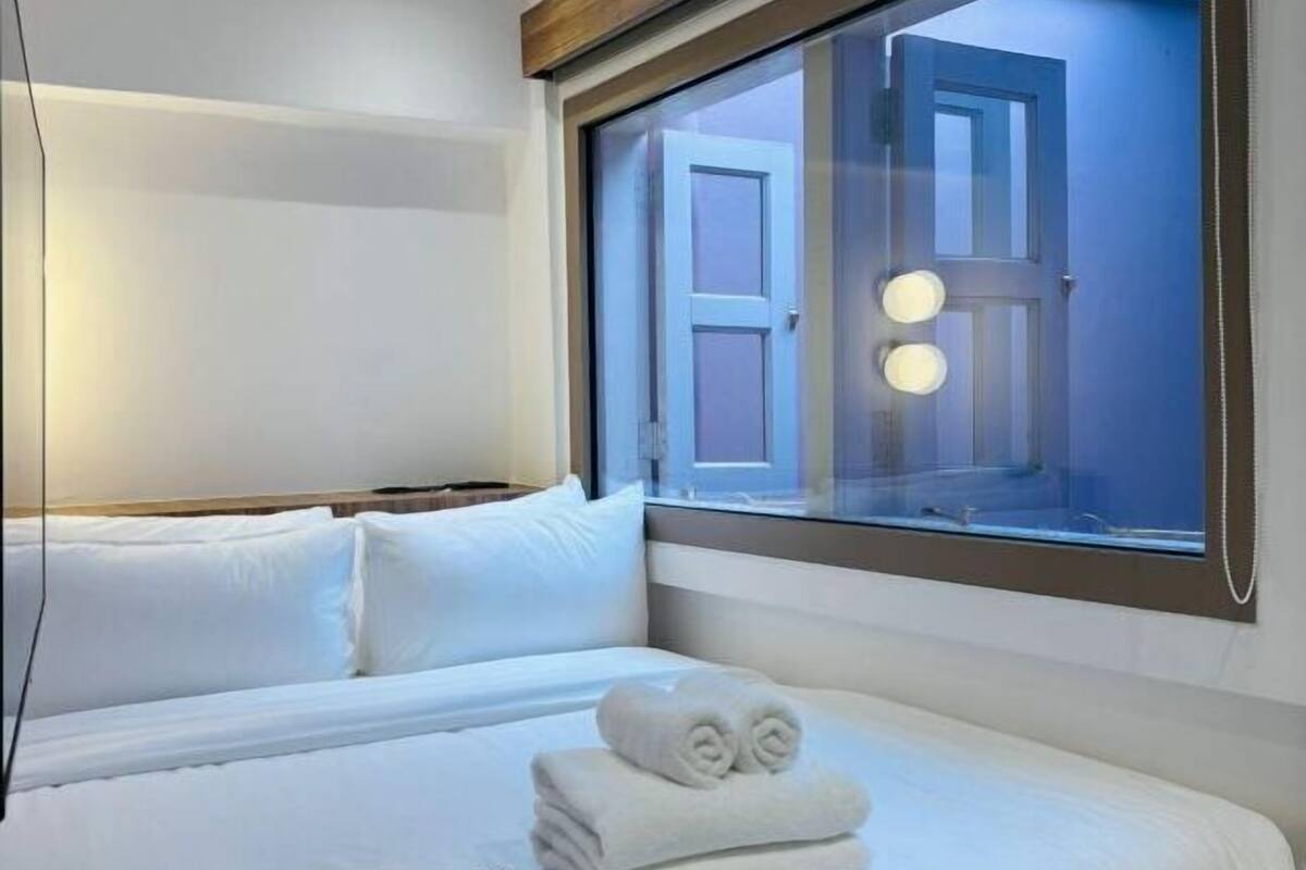 A hotel room with a bed, a window with a view of the outside, and a door.