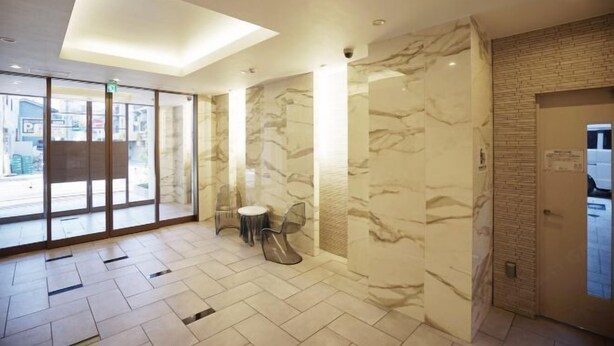 A modern hotel lobby with marble walls, a glass entrance, and a small seating area. - Chuan House Kuromon (Osaka)