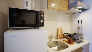A compact kitchen with a microwave on top of a white refrigerator, a sink, and a wooden cutting board. - Chuan House Kuromon (Osaka)