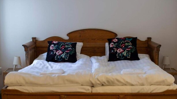 A double bed with a wooden headboard, two black pillows with floral designs, white bedding, and two bedside lamps on wooden nightstands. - 2 Person Holiday Park Home in 82011 (Vallsta)