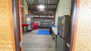 Un couloir étroit avec un tapis bleu, une poubelle rouge et un réfrigérateur.
