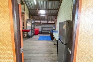 Un couloir étroit avec un tapis bleu, une poubelle rouge et un réfrigérateur.