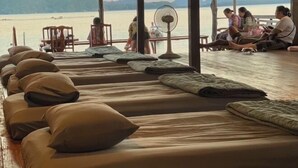 Reihe von Betten mit Kissen, ein Ventilator und Blick auf ein Gewässer und Berge.