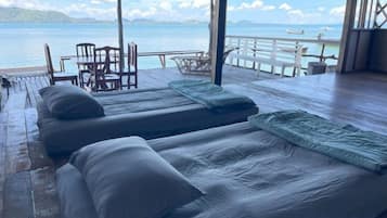 Una habitación con dos camas, piso de madera, una mesa, sillas y vista al mar.