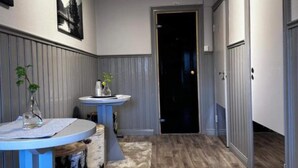 A hallway with a round blue table and a small white table, both with vases and a plant. The walls are paneled, and there's a door at the end. - 4 Person Holiday Park Home in 82011 (Vallsta)