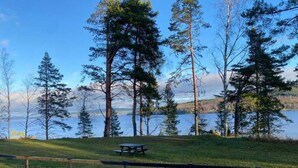 A picnic table in a grassy area with a lake and trees in the background. - 4 Person Holiday Park Home in 82011 (Vallsta)