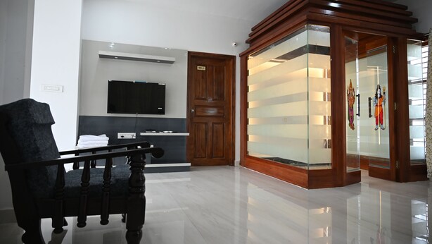 A modern hotel room with a flat-screen TV, a wooden door, and a glass partition with decorative elements. - Surya-Atharva Suites (Mysore)