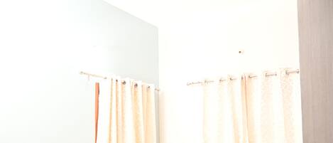 A bedroom with a bed, curtains, a ceiling fan, and a door.