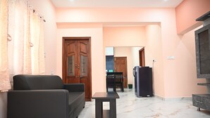 A living room with a sofa, a small table, a TV, and a wooden door. - Surya-Atharva Suites (Mysore)