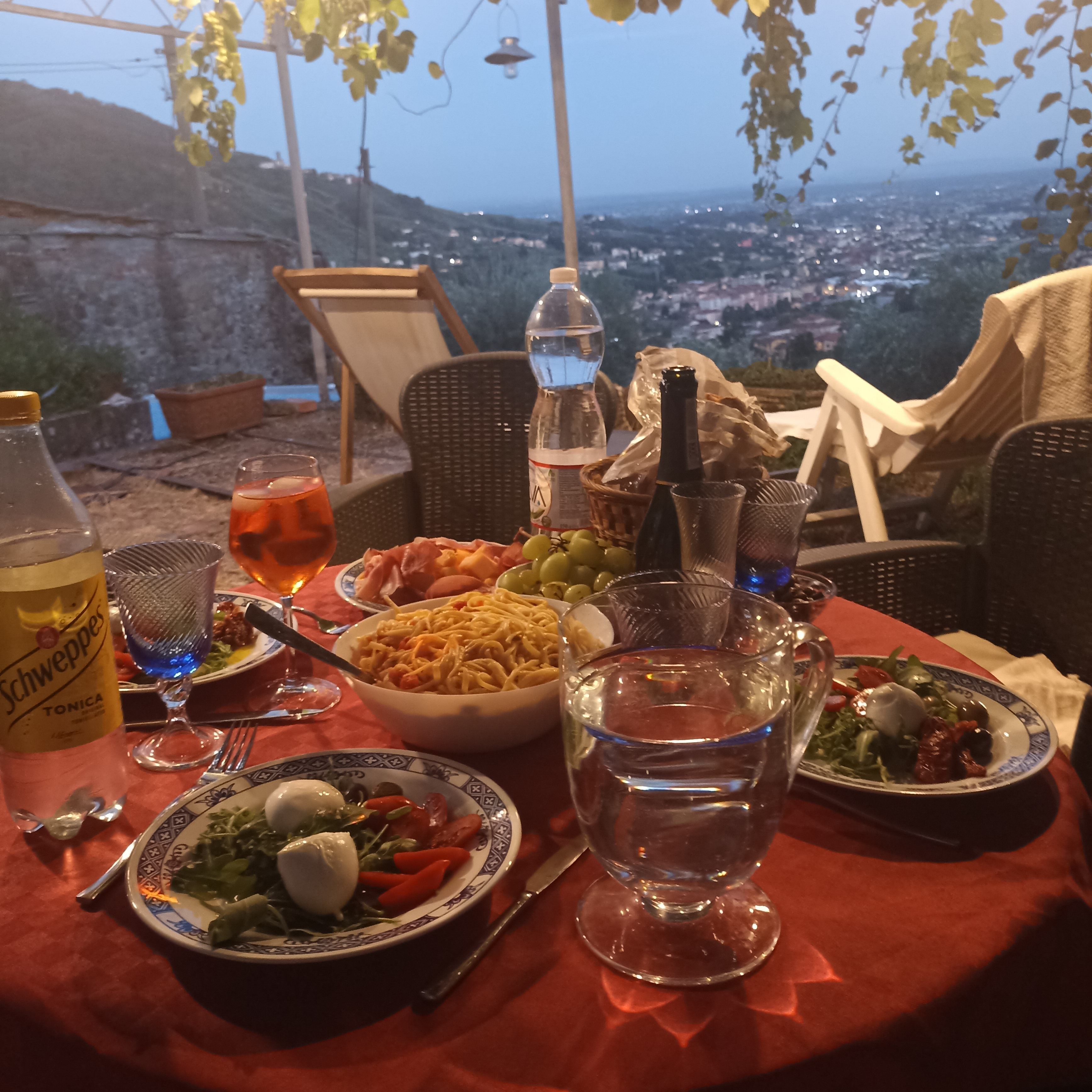 A table set with a variety of dishes, including pasta, salad, and a bottle of water, with a scenic view in the background.