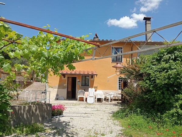 A house with a tiled roof, a wooden door, and a small patio with white plastic chairs and a table.