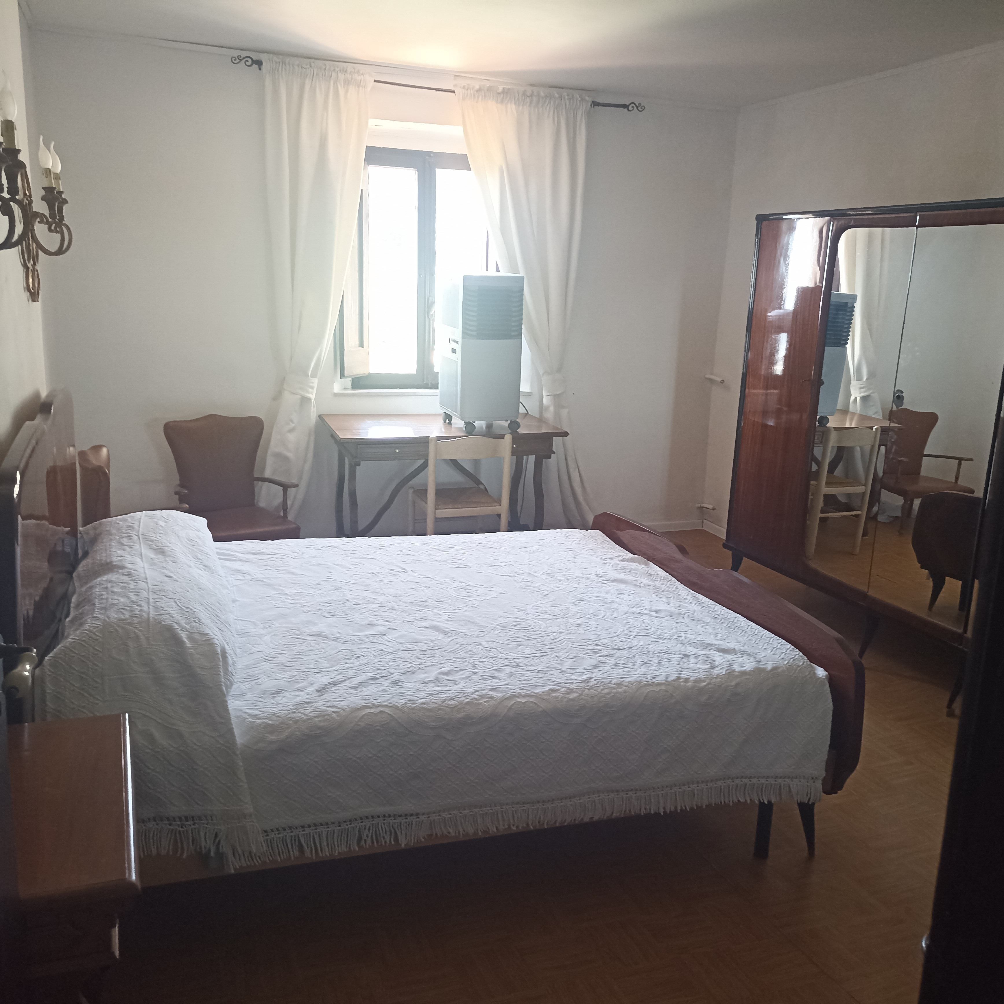 A hotel room with a bed, a desk, a chair, a mirror, and a window with curtains.