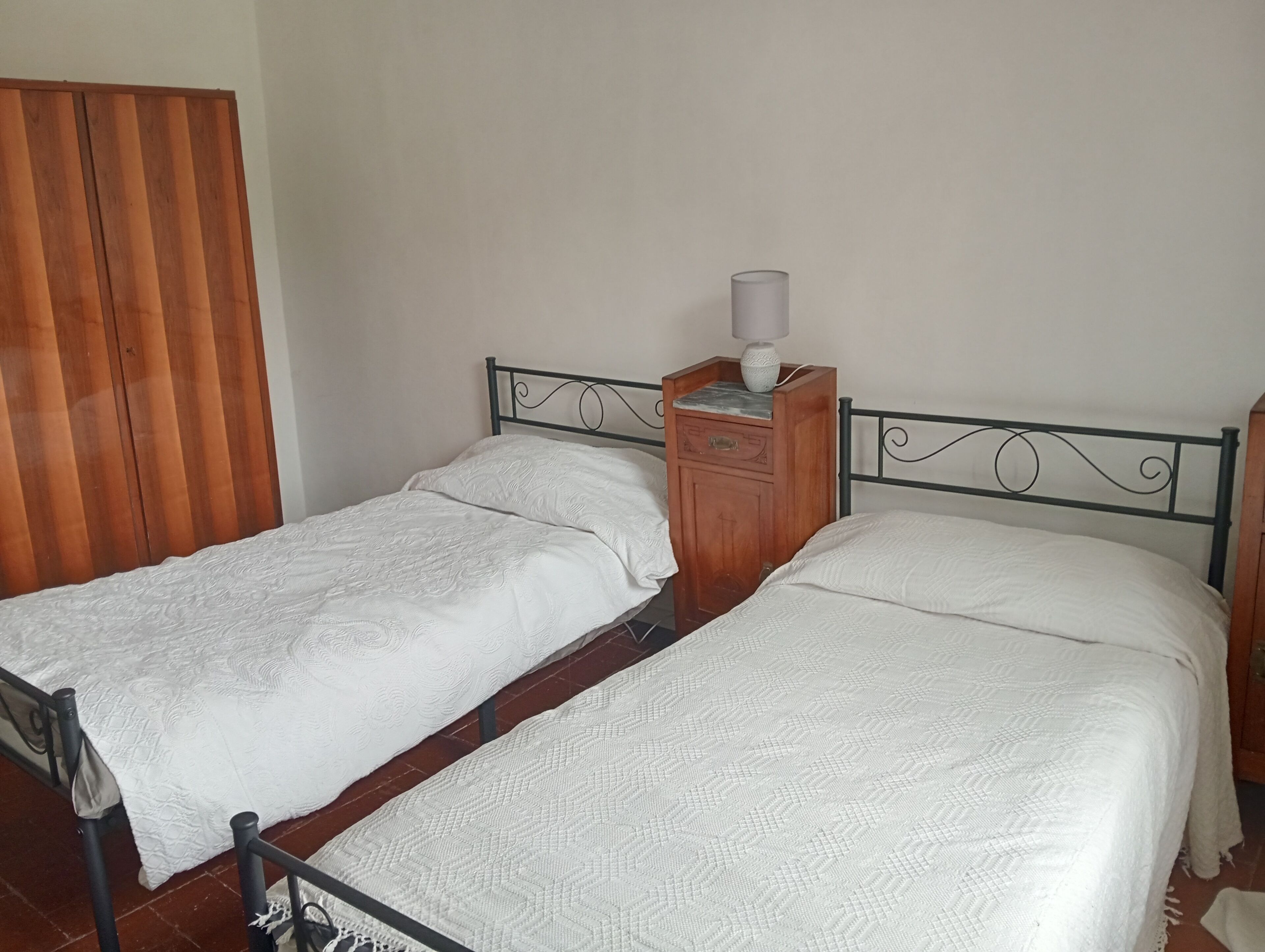 Ein Schlafzimmer mit zwei Einzelbetten, einem Holzschrank und einem Nachttisch mit Lampe.