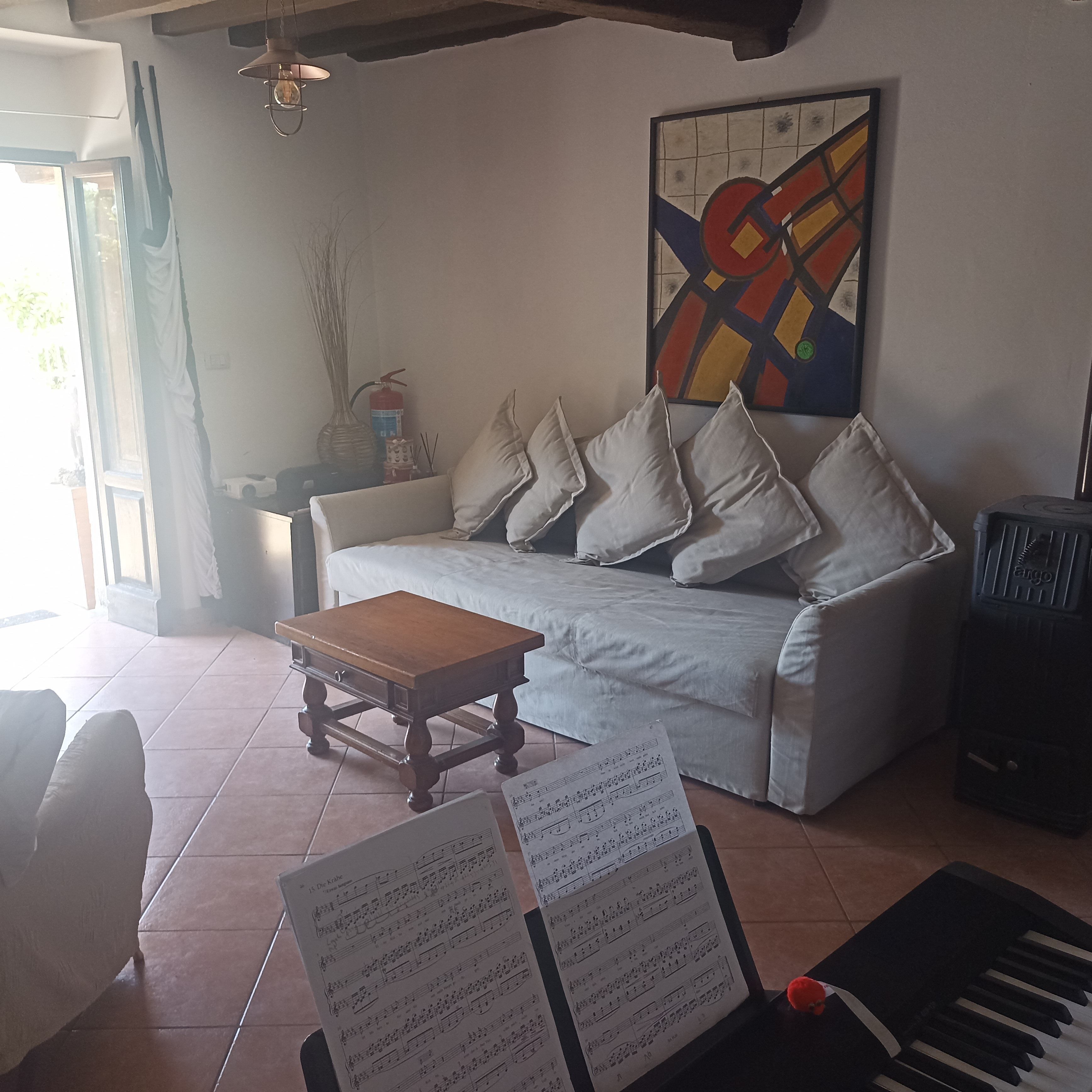 Ein Wohnzimmer mit einer Couch, einem kleinen Holztisch, einem Klavier und einem Fenster mit Vorhängen.