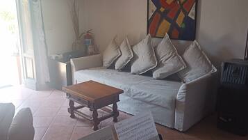 Ein Wohnzimmer mit einer Couch, einem kleinen Holztisch, einem Klavier und einem Fenster mit Vorhängen.