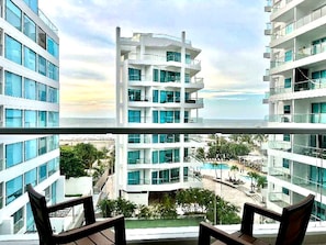 A high-rise hotel with multiple balconies, a pool area, and a view of the ocean.