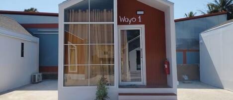 A small, modern building with a sign reading 'Wayo 1' and a potted plant in front.