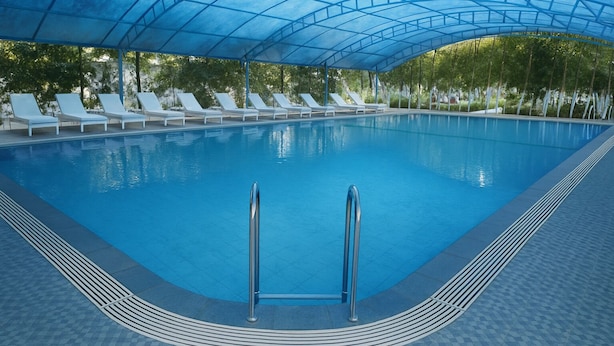 Une piscine intérieure à l’eau d’un bleu cristallin, entourée de chaises longues blanches et surmontée d’un auvent bleu.