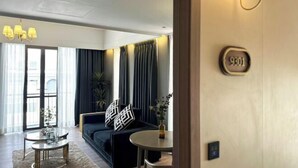 Una habitación de hotel moderna con sofá, una mesa redonda, una araña y un ventanal grande.