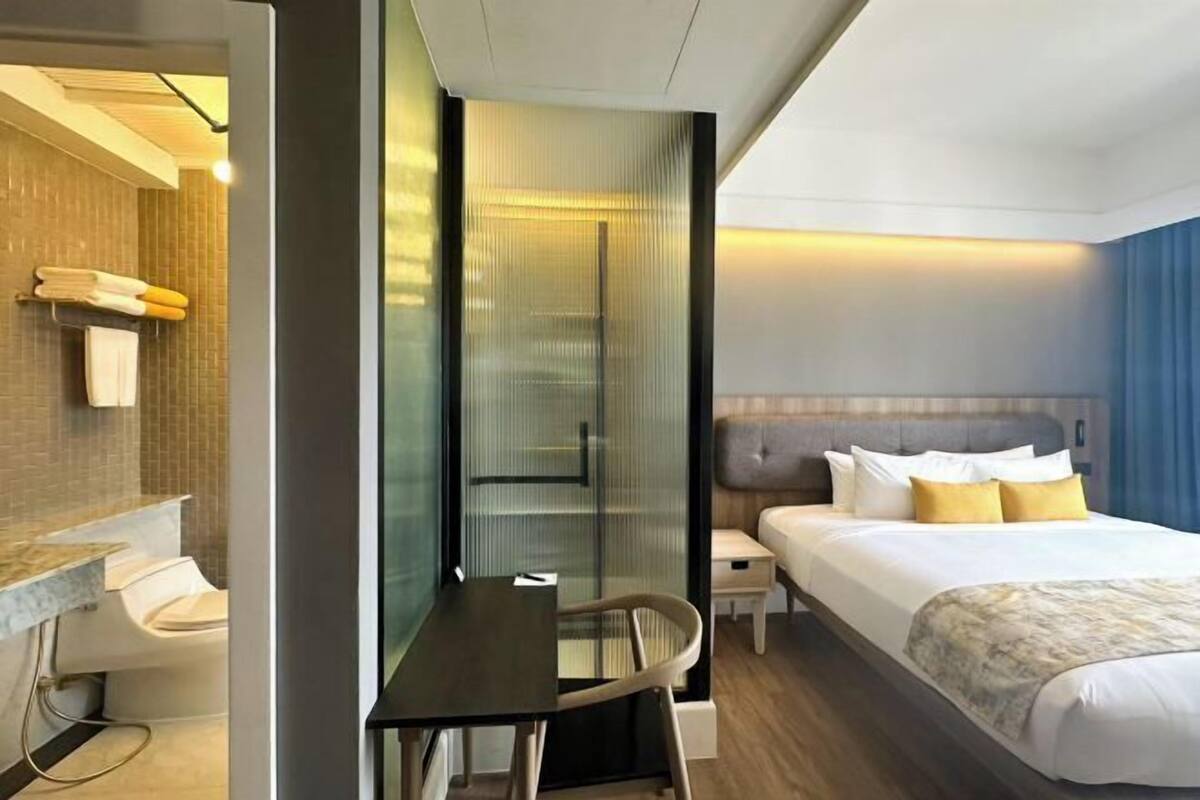 Une chambre d’hôtel comprenant un lit, une table de chevet, une chaise et une cloison en verre qui sépare la salle de bain de la chambre.