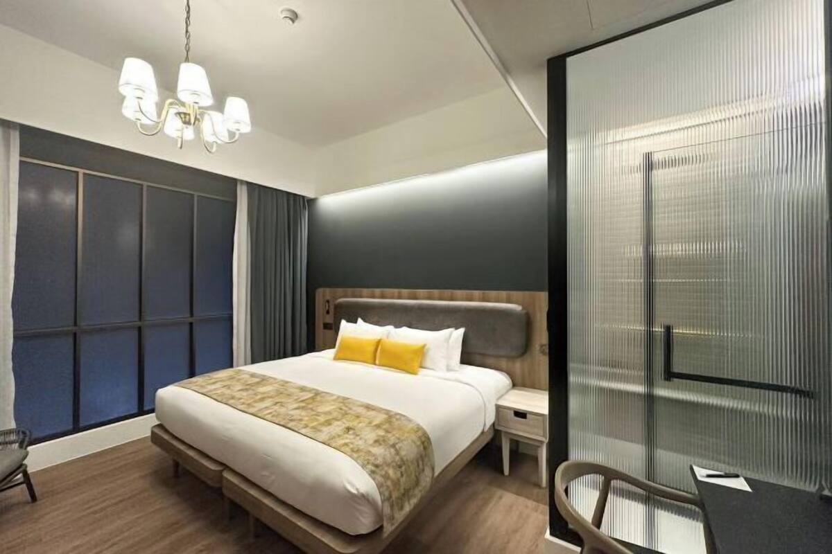 Une chambre d’hôtel moderne avec un grand lit, une table de chevet, une chaise et une grande fenêtre avec des rideaux.