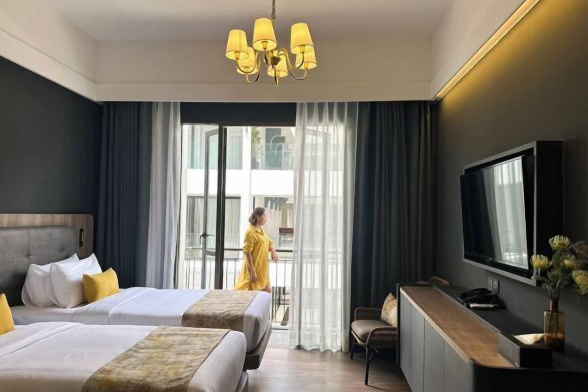 Une chambre d’hôtel avec deux lits, une télévision, un bureau et une grande fenêtre avec des rideaux.