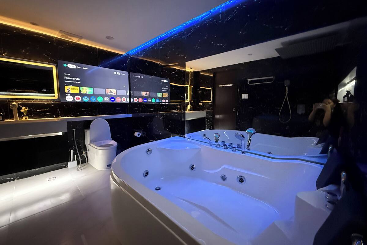 A modern bathroom with a large bathtub, a vanity with a mirror, and a digital display wall.