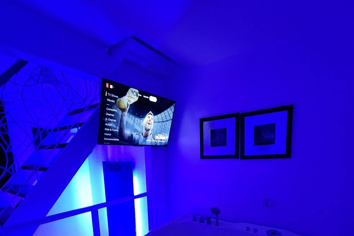 A modern bathroom with a large bathtub, a TV mounted on the wall, and framed pictures on the wall.