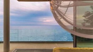 A balcony with a view of the sea, a bed with a yellow cover, and a glass partition.