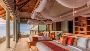 A bedroom with two beds, a view of the sea, and a wooden ceiling.