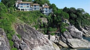 A coastal property with multiple buildings, rocky terrain, and dense greenery.