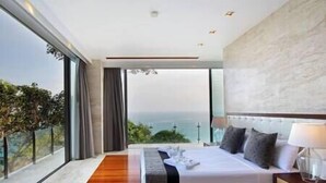 A modern hotel room with a large bed, a view of the ocean, and a balcony with curtains.