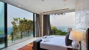 A modern hotel room with a large bed, a bedside lamp, and a view of the ocean.