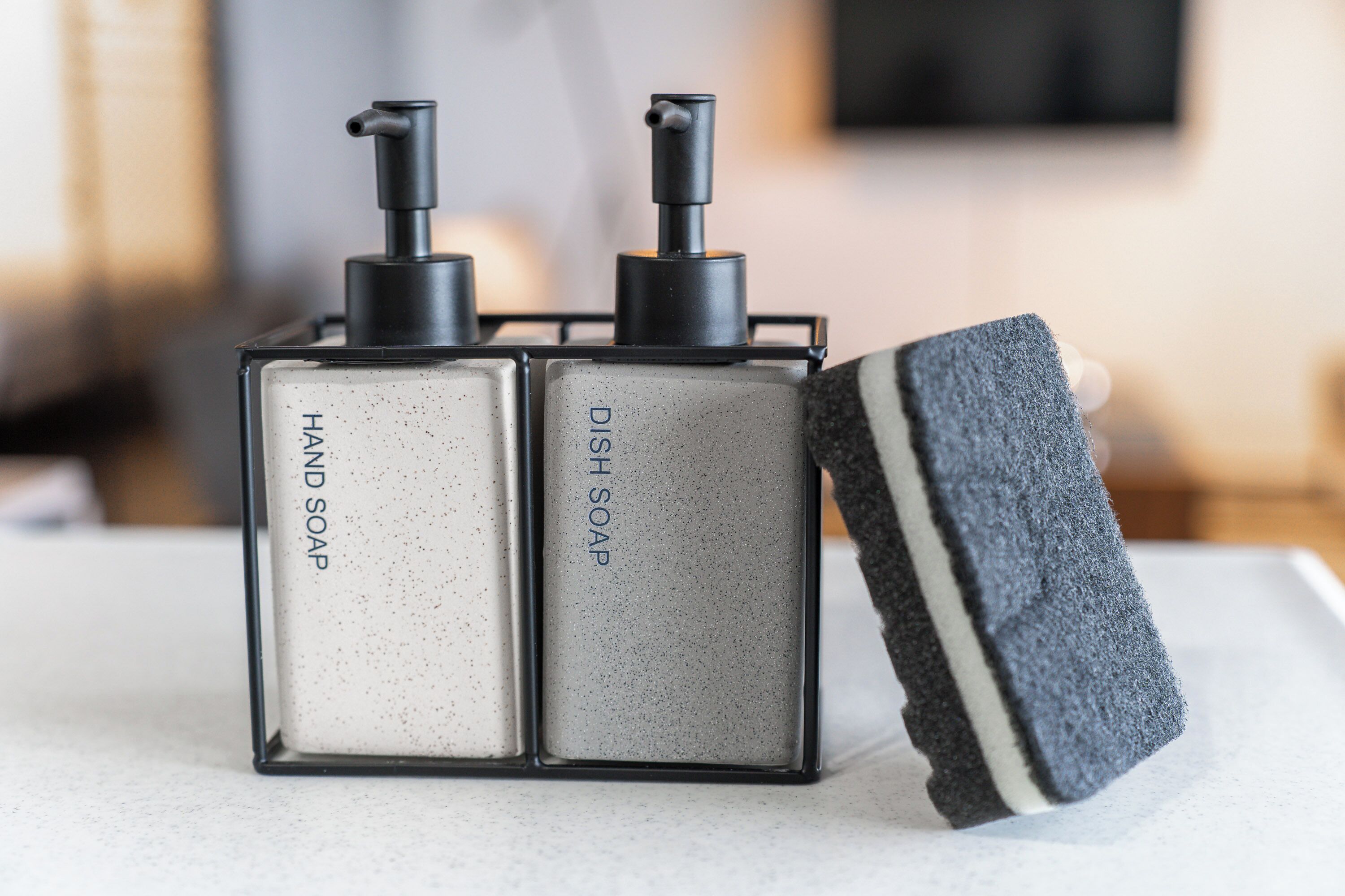 Two soap dispensers and a sponge on a countertop.