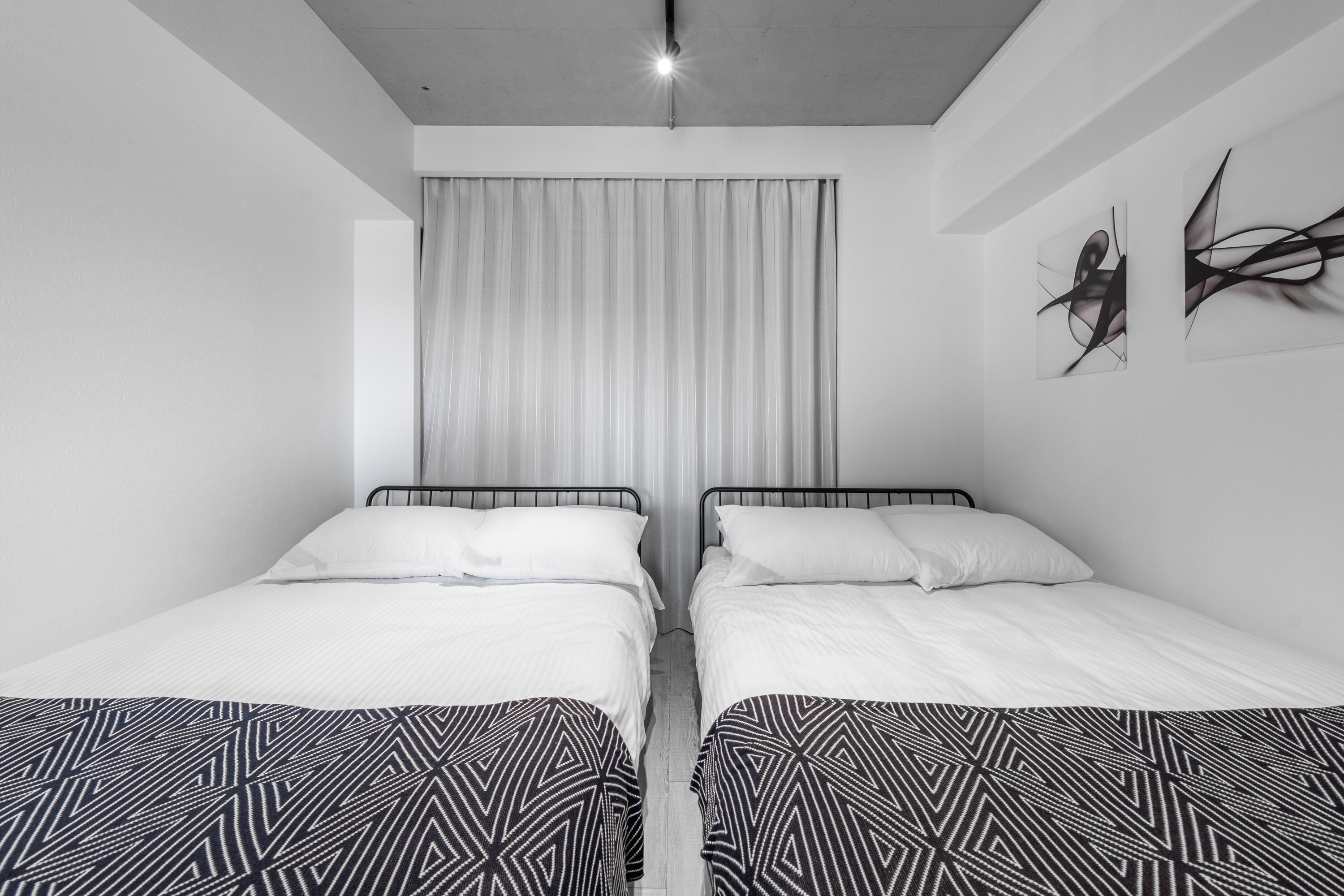Une chambre d’hôtel moderne avec deux lits simples, une grande fenêtre avec des rideaux et des œuvres d’art abstraites sur les murs.