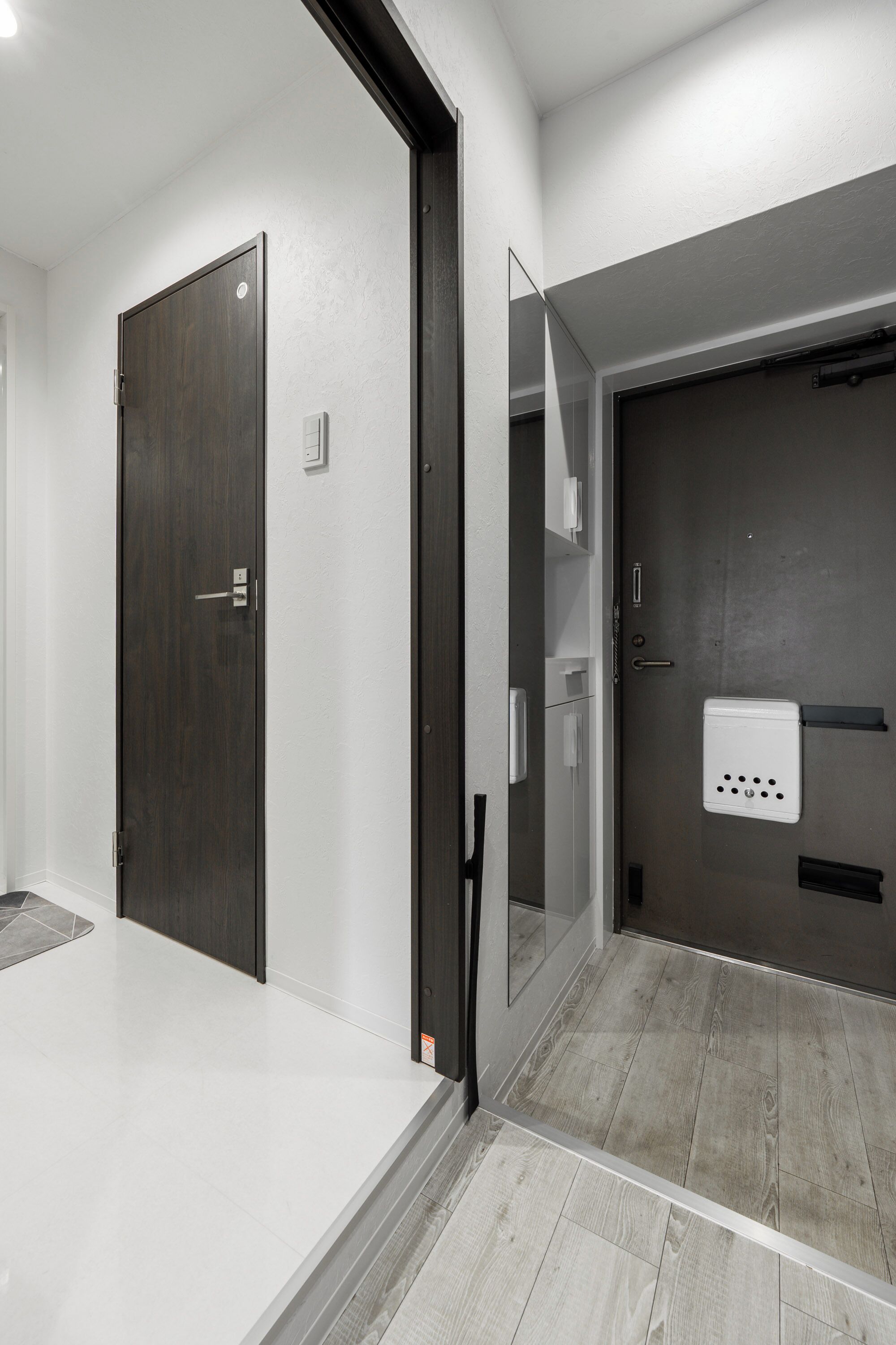 A modern hotel room with a large mirror, a dark wooden door, and a light-colored floor.