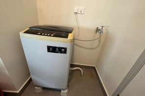 A compact, white laundry machine with a control panel, connected to a wall socket. - JazzA Suite by Homey Planet (Tanjung Tokong)