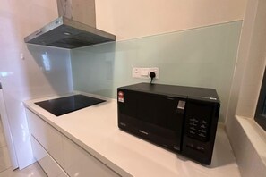 A kitchen with a black microwave, a glass backsplash, and a white countertop. - JazzA Suite by Homey Planet (Tanjung Tokong)