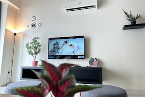 A modern living room with a flat-screen TV mounted on the wall, a potted plant, and a black entertainment unit. - JazzA Suite by Homey Planet (Tanjung Tokong)