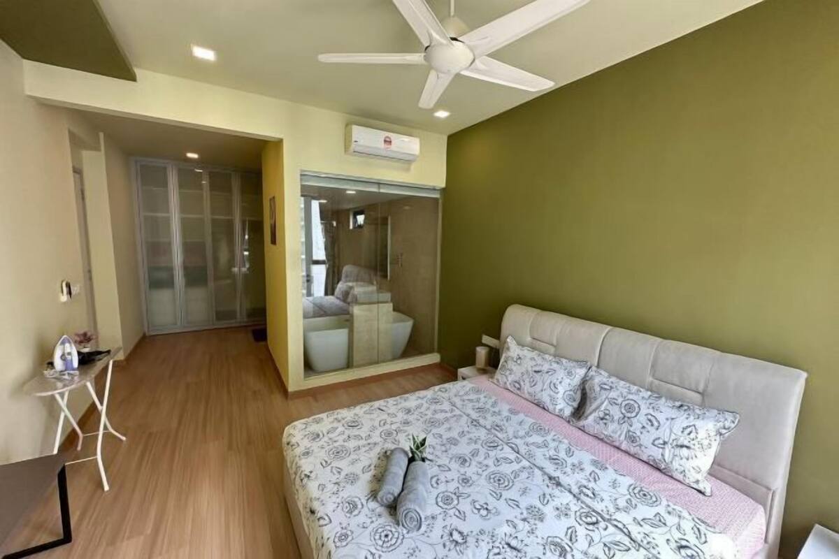 A bedroom with a bed, a ceiling fan, a small table, and a glass-enclosed shower area.