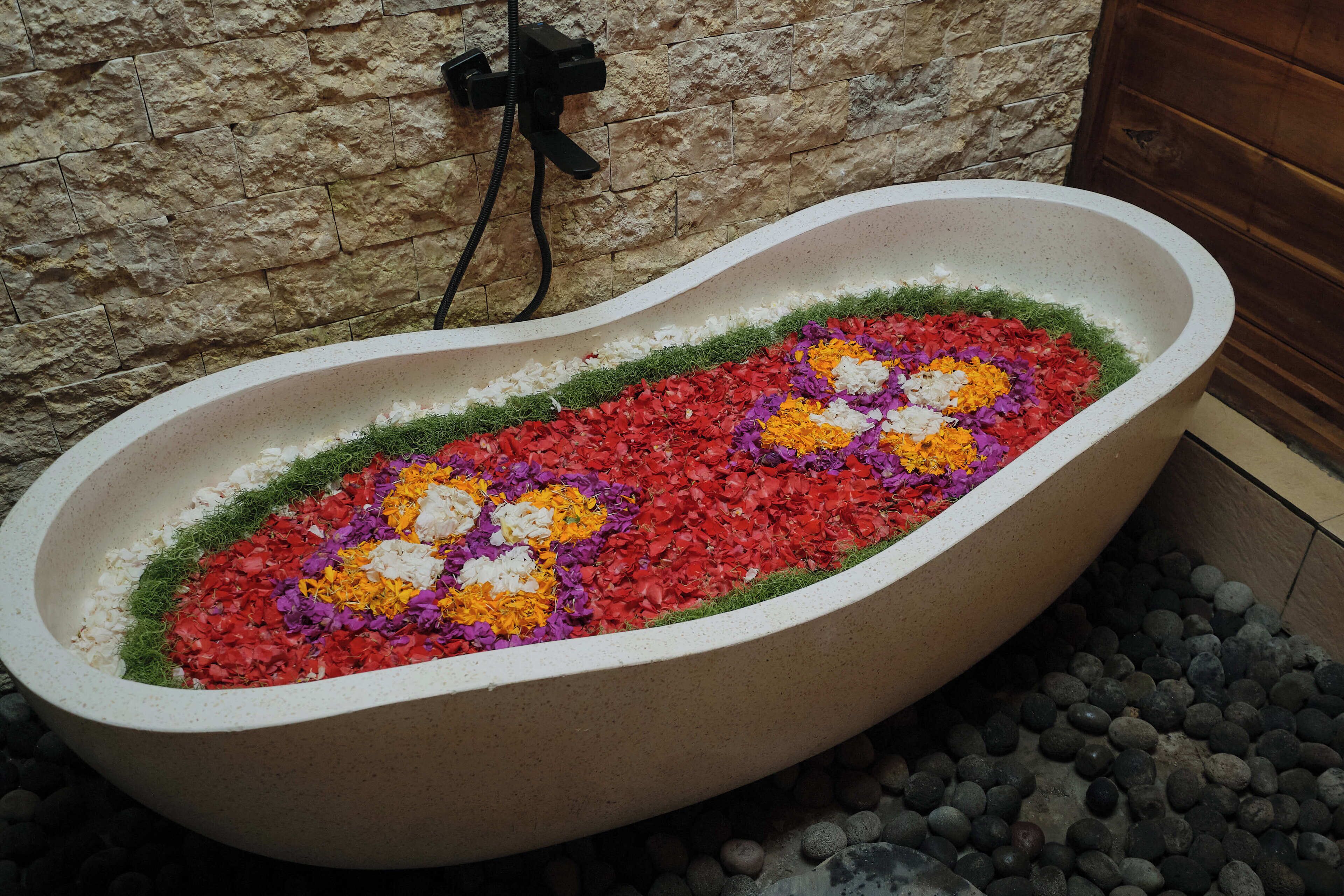 A bathtub filled with colorful flower petals and surrounded by a stone wall.