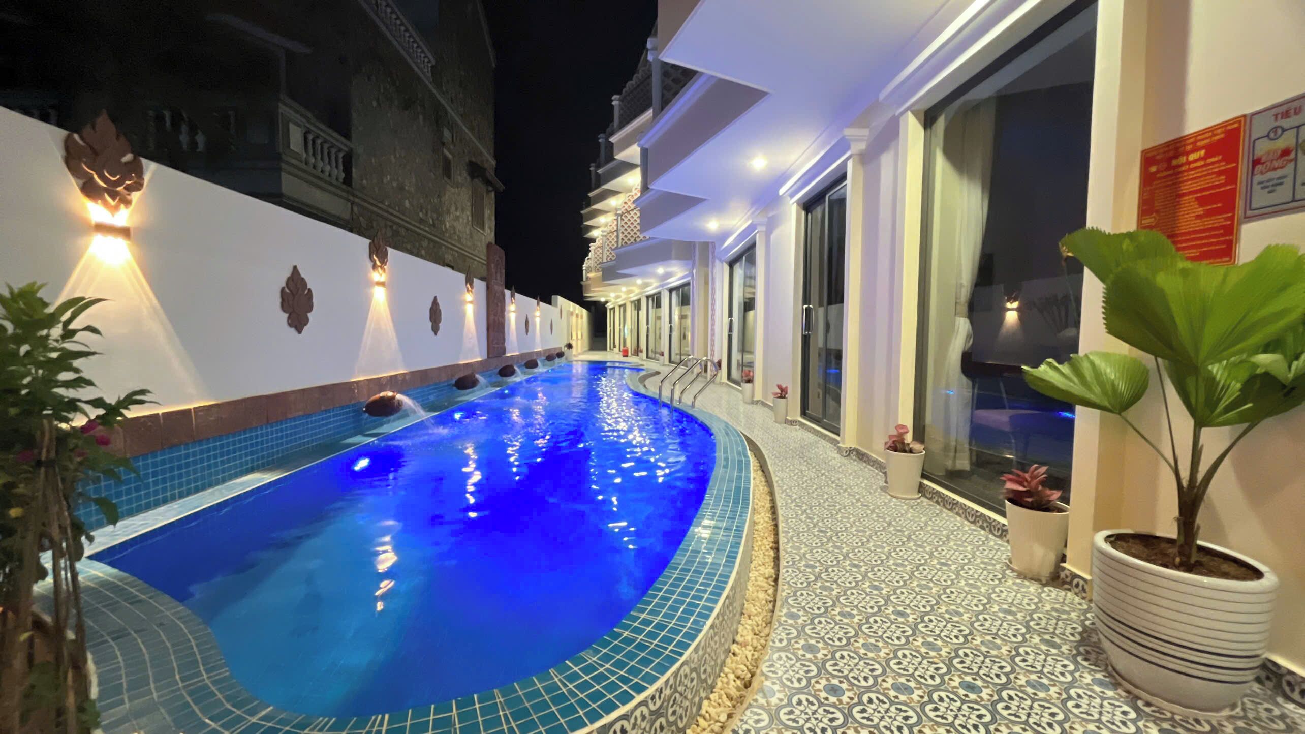A swimming pool with a tiled edge, surrounded by a white building with decorative lighting.