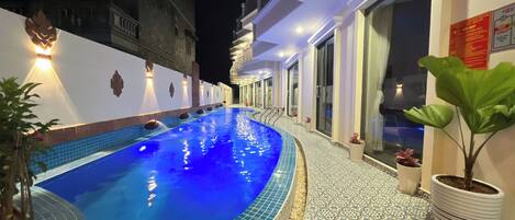 A swimming pool with a tiled edge, surrounded by a white building with decorative lighting.