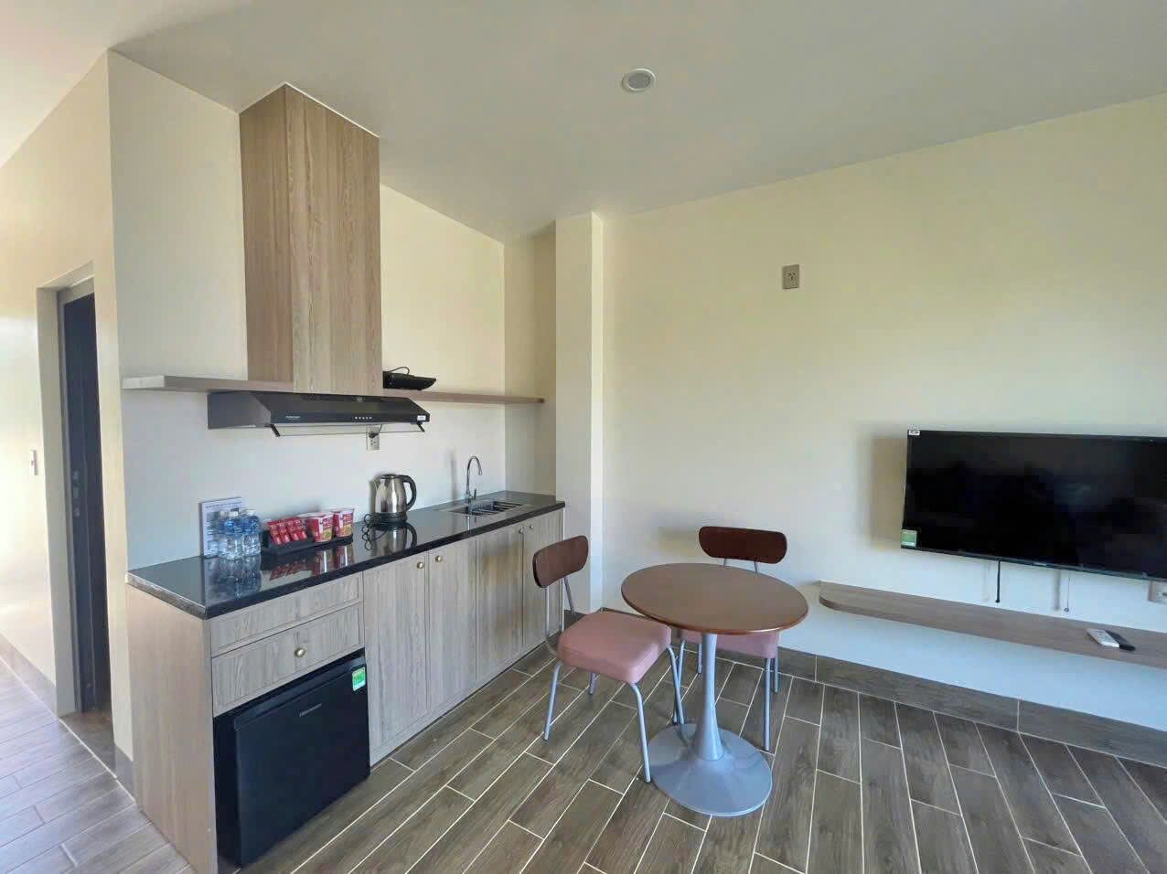 Una cocina moderna con horno empotrado, cafetera y lavaplatos. Hay una zona de comedor con una mesa redonda y dos sillas. Un televisor de pantalla plana está montado en la pared sobre la mesa.