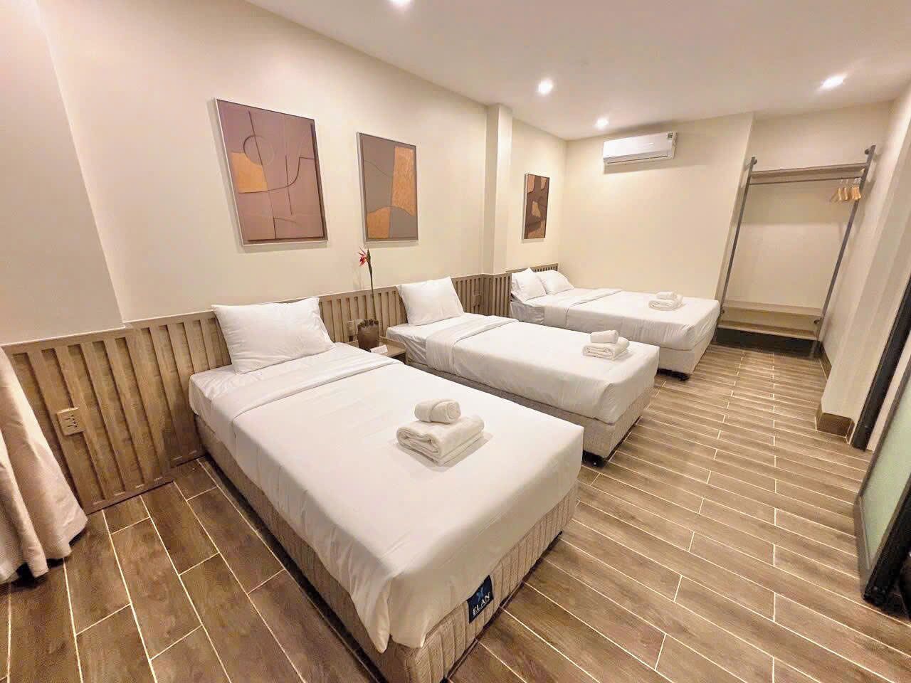 A hotel room with three single beds, a wooden floor, and a shower area.